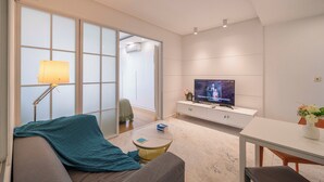 Una sala de estar moderna con un sofá, una mesa de centro, un televisor y un ventanal corredera que da a un balcón.