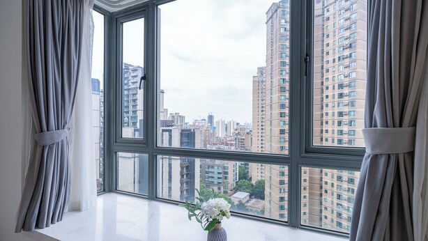 Una habitación con un ventanal grande, cortinas y un florero con flores en el alféizar.