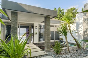 Una casa moderna con piscina, pilares de piedra y plantas tropicales.