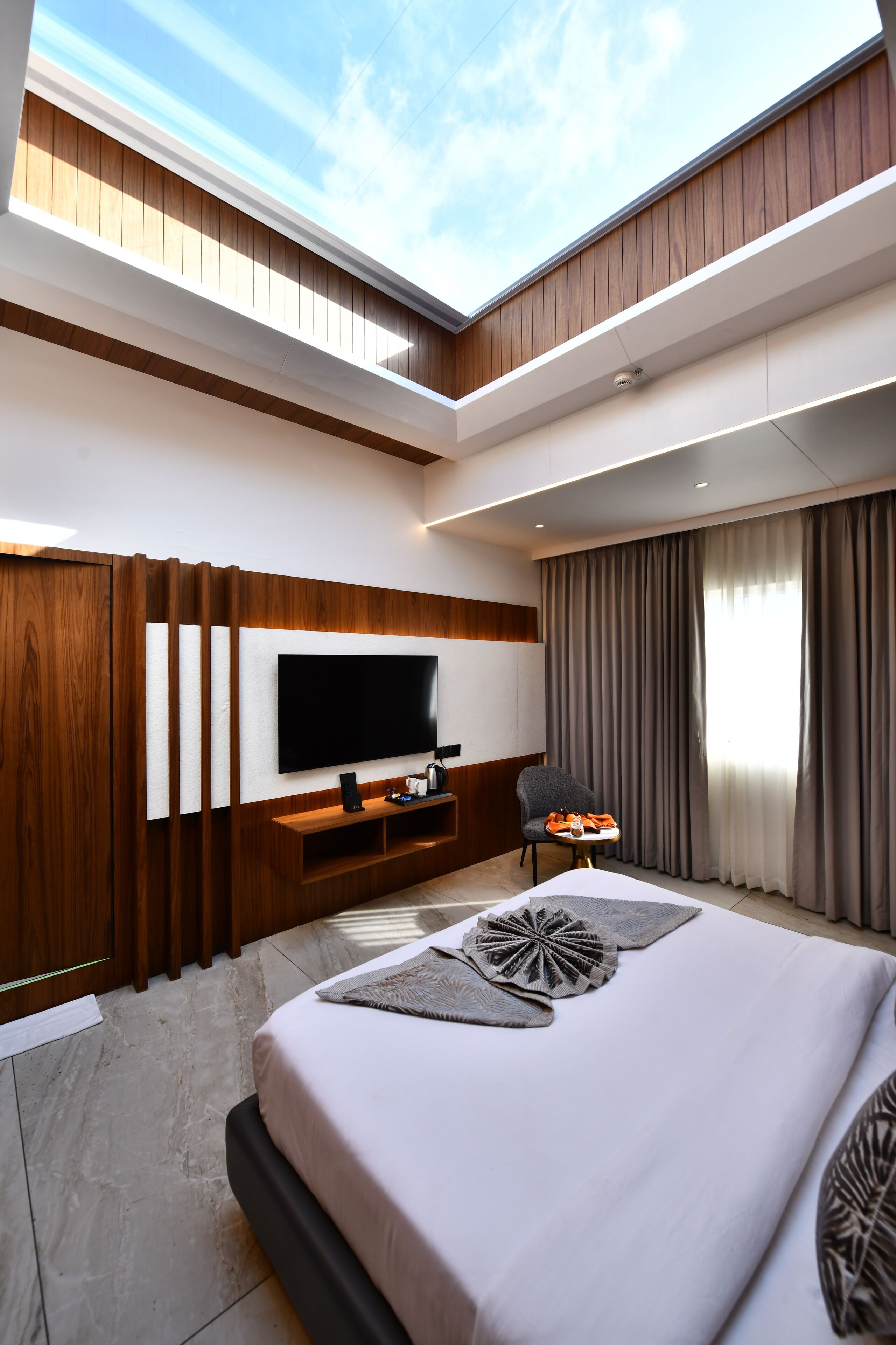 Une chambre d’hôtel moderne dotée d’un grand lit, d’un téléviseur à écran plat, d’un coin salon et offrant une vue sur le ciel grâce à une ouverture dans le plafond.