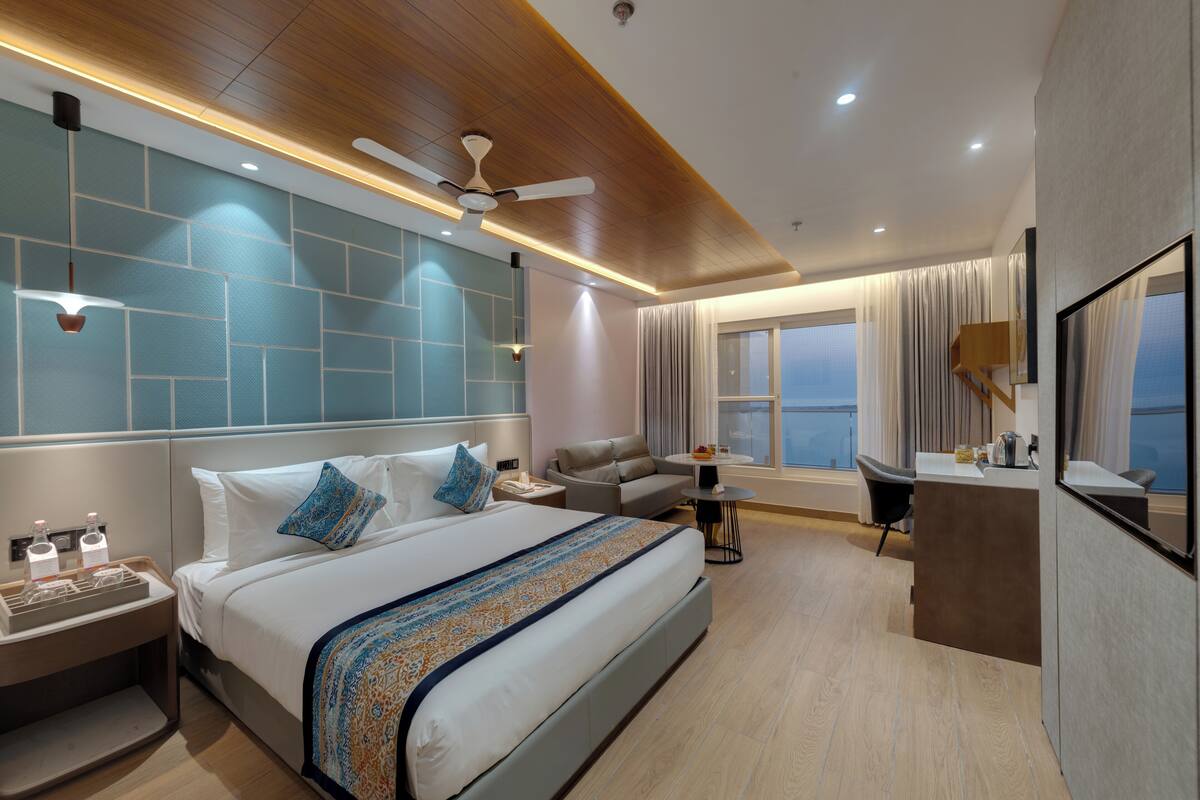 A modern hotel room with a large bed, a sofa, a desk, and a balcony view.