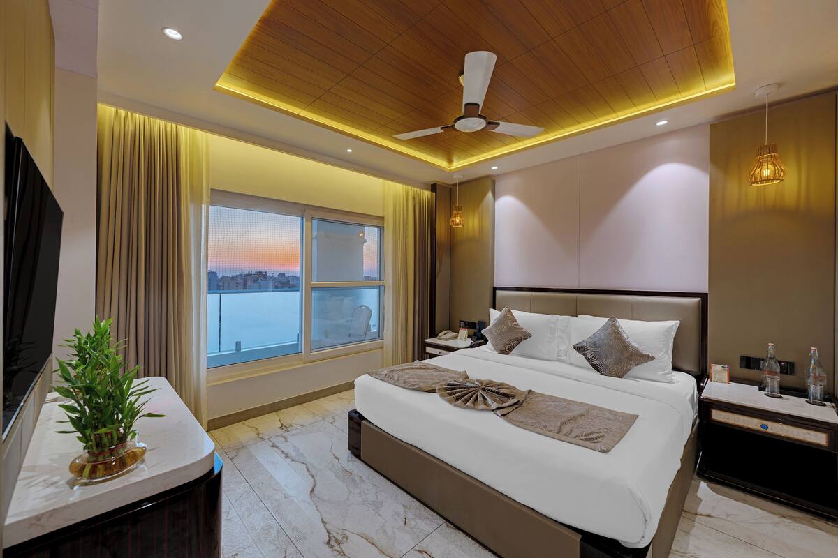 A modern hotel room with a large bed, a ceiling fan, a nightstand, a bedside table, and a window with a view.