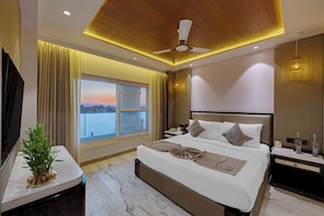 Una habitación de hotel moderna con una cama grande, un ventilador de techo, una mesita de noche y un ventanal con vistas.