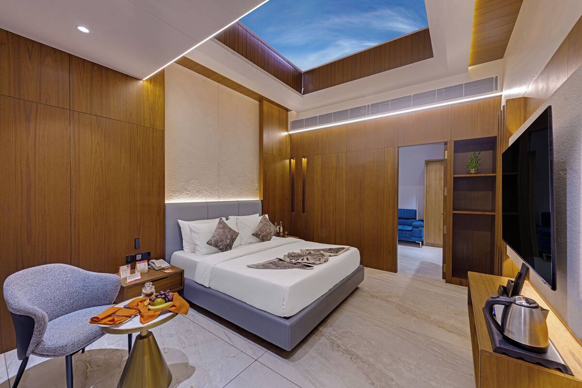 A modern hotel room with a bed, a seating area, a TV, and a skylight.