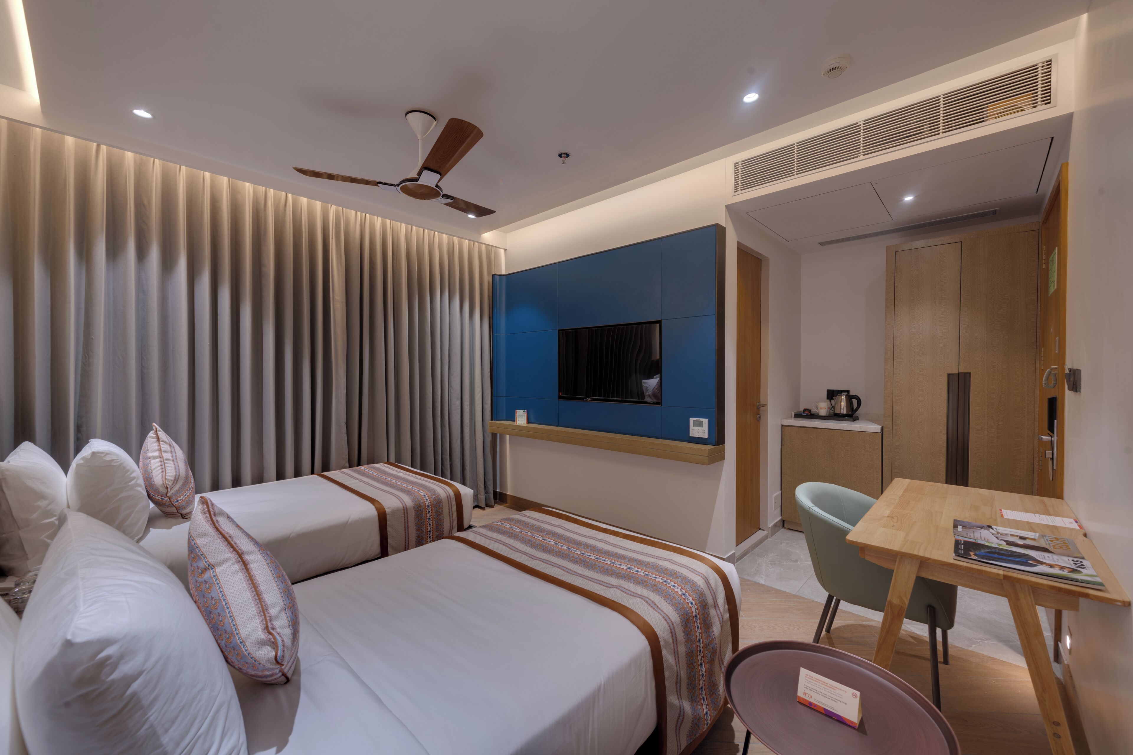 Habitación de hotel con dos camas, un escritorio, una silla, un televisor y un ventilador de techo.