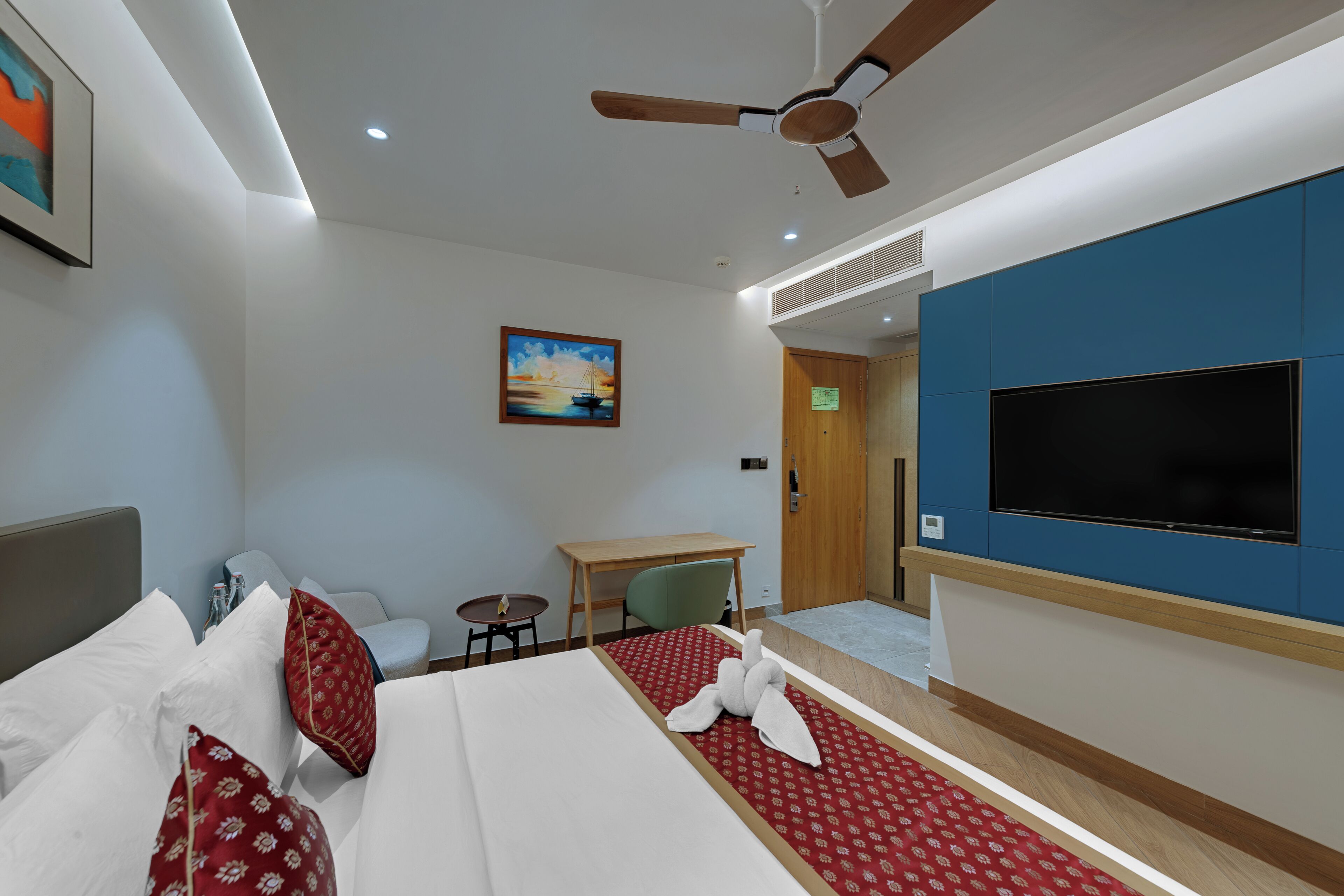 Habitación de hotel con una cama, un escritorio, una silla, un televisor y un ventilador de techo.