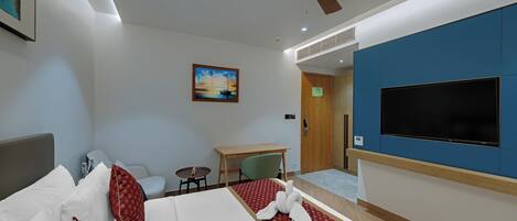 A hotel room with a bed, a desk, a chair, a television, and a ceiling fan.