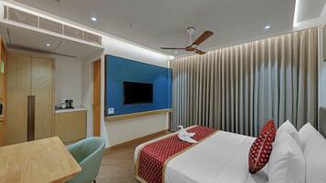 Una habitación de hotel con una cama, un televisor en la pared, un ventilador de techo y una mesa de madera.