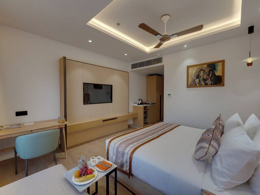 A hotel room with a bed, desk, chair, and a painting on the wall.