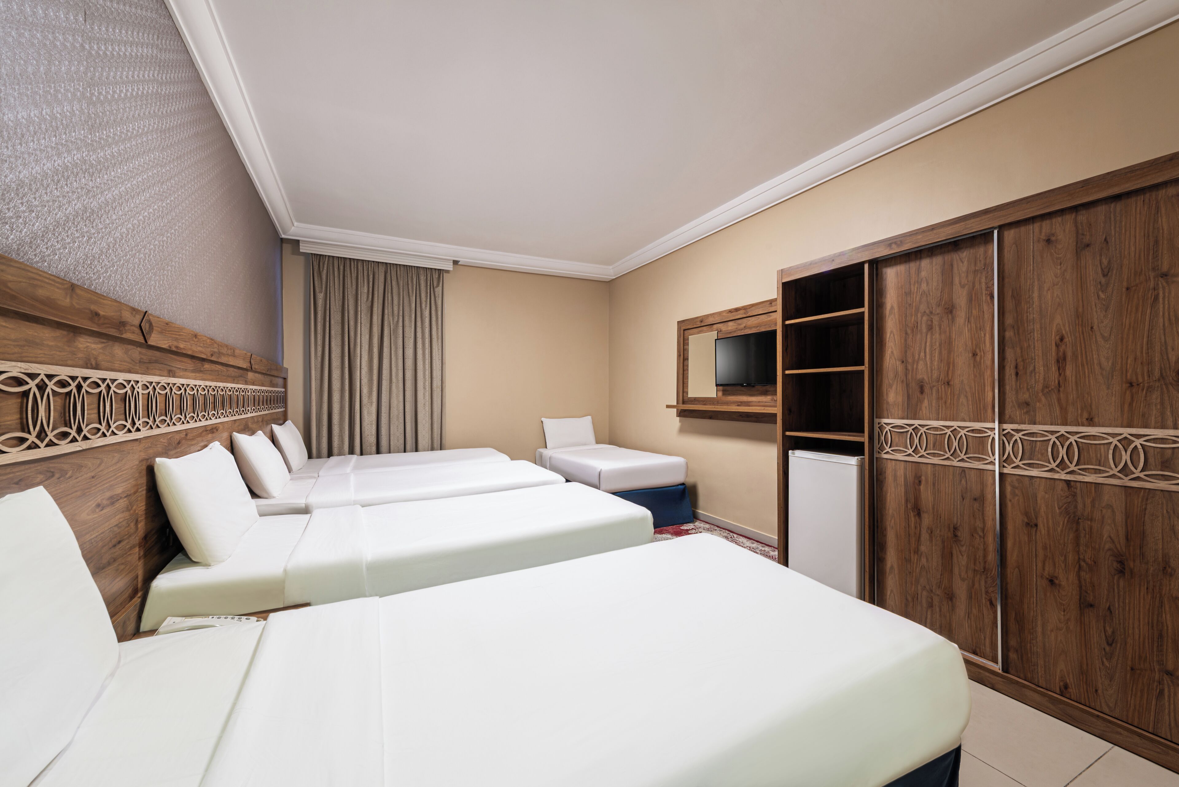 A hotel room with two beds, a TV, a wardrobe, and a small table.