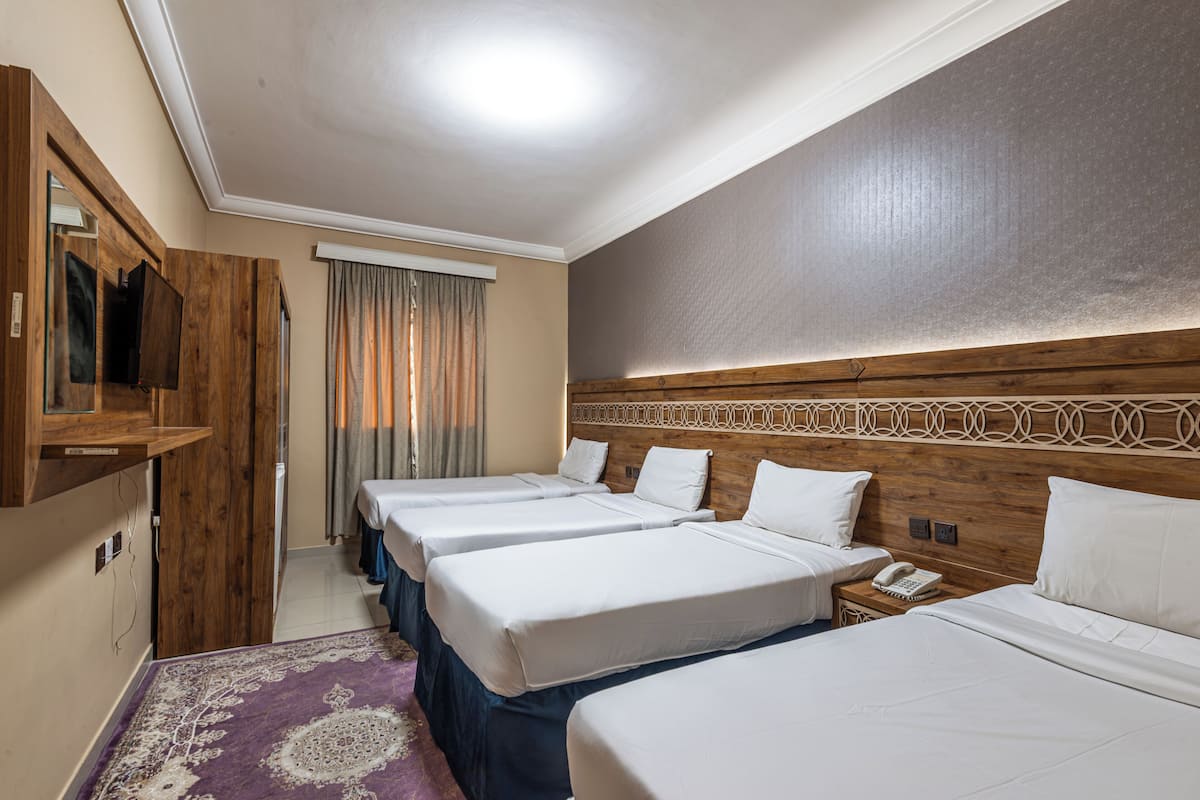 A hotel room with four single beds, a wooden headboard, a small bedside table with a phone, and a purple patterned rug.