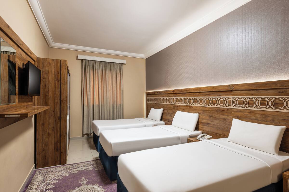 A hotel room with two beds, a wooden headboard, a flat-screen TV, and a bathroom with a shower curtain.