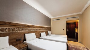 A hotel room with three beds, a wooden headboard, a patterned rug, and a door leading to a hallway. - Razana Al Hafayyer (Makkah)