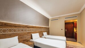 A hotel room with two single beds, a wooden headboard, a small bedside table with a phone, and a door leading to a bathroom. - Razana Al Hafayyer (Makkah)
