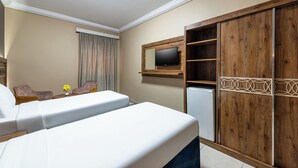 A hotel room with a bed, two chairs, a TV mounted on a wooden panel, and a small refrigerator. - Razana Al Hafayyer (Makkah)