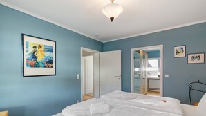 A bedroom with a bed, a framed painting, and a door leading to a bathroom.
