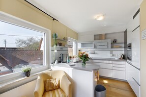 Una cocina moderna con armarios blancos, microondas integrado y ventana con vista a fachada de ladrillo.