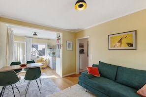 Un salon avec un canapé, une table à manger et des chaises, un coin cuisine et une porte donnant sur une autre pièce.