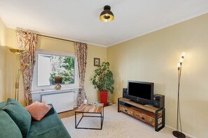 Una sala de estar con un sofá, una mesa de centro, un televisor, una lámpara de pie y una ventana con cortinas.