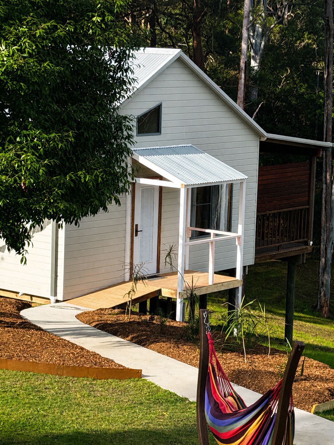 A small white house with a porch, surrounded by trees and a hammock.