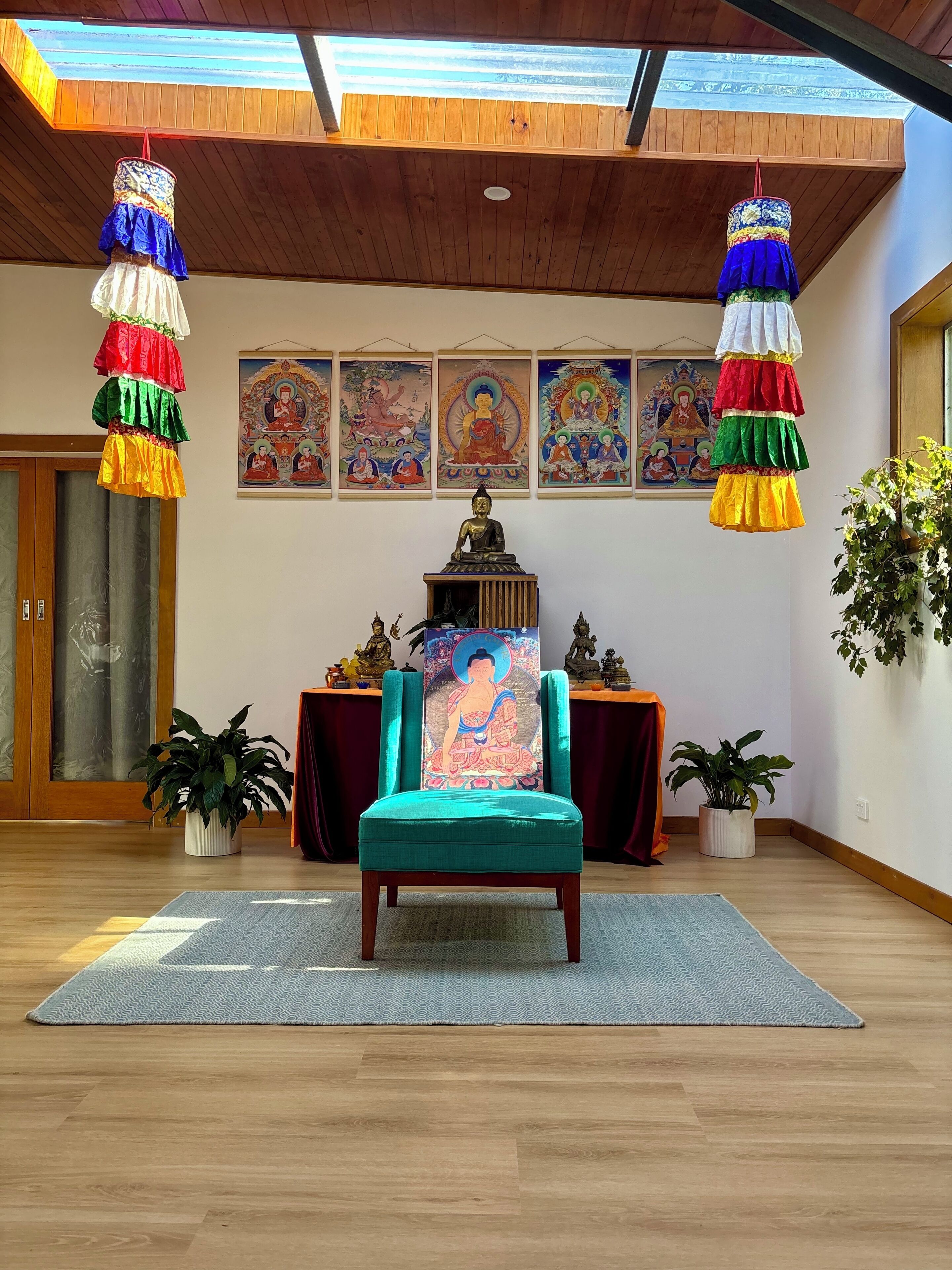 Una habitación con techo de madera, un sillón con cojines verdes, una estatua de Buda y decoraciones colgantes de colores.