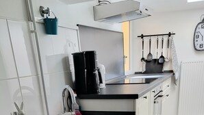Une cuisine moderne avec des meubles blancs, un lave-vaisselle encastré, une machine à café et un étendoir suspendu pour les ustensiles.