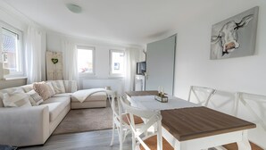 Un salon moderne comprenant un canapé, une table à manger, des chaises, un téléviseur et un tableau.