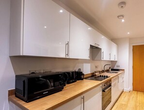 Une cuisine moderne avec des meubles blancs, un plan de travail en bois, une machine à café, une bouilloire et une cuisinière.