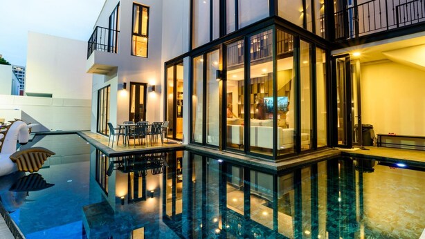 Una casa moderna con un espacio de estar con paredes de vidrio, piscina y balcón.