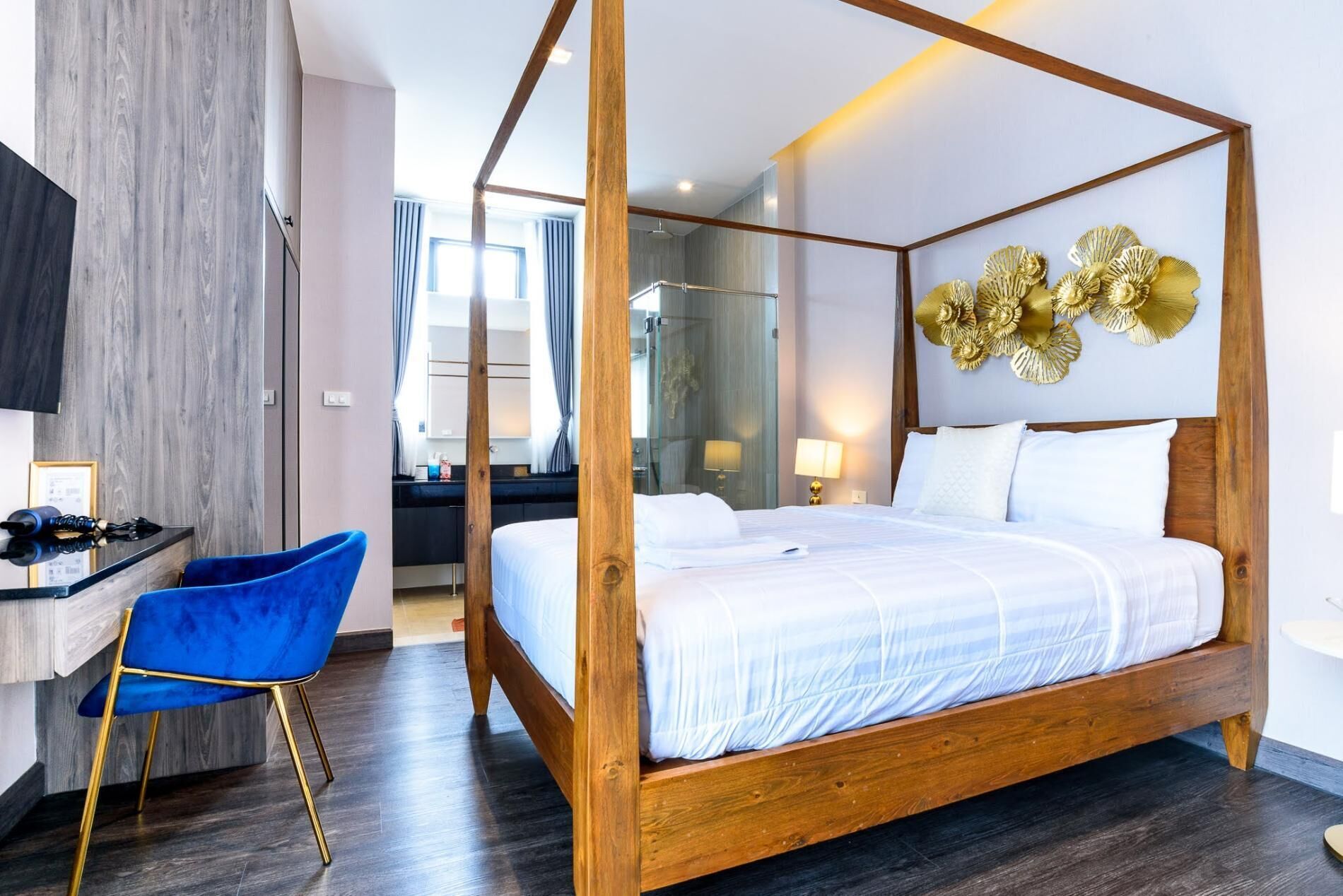 A four-poster bed with a wooden frame and white bedding, a blue chair with gold legs, and a wall-mounted decorative piece.