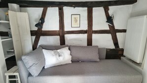 A grey sofa with pillows, a white radiator, and a framed picture on a wall with exposed beams. - Apartment 'Snug' with Wi-Fi (Neuenstein)