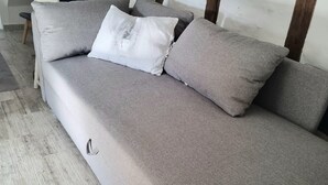 A grey sofa with a white pillow, a wooden ladder, and a framed picture on the wall. - Apartment 'Snug' with Wi-Fi (Neuenstein)