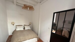 A bedroom with a bed, two wall-mounted lamps, a ceiling fan, and a door leading to another room. - Authentique Bouquet (Le Mans)