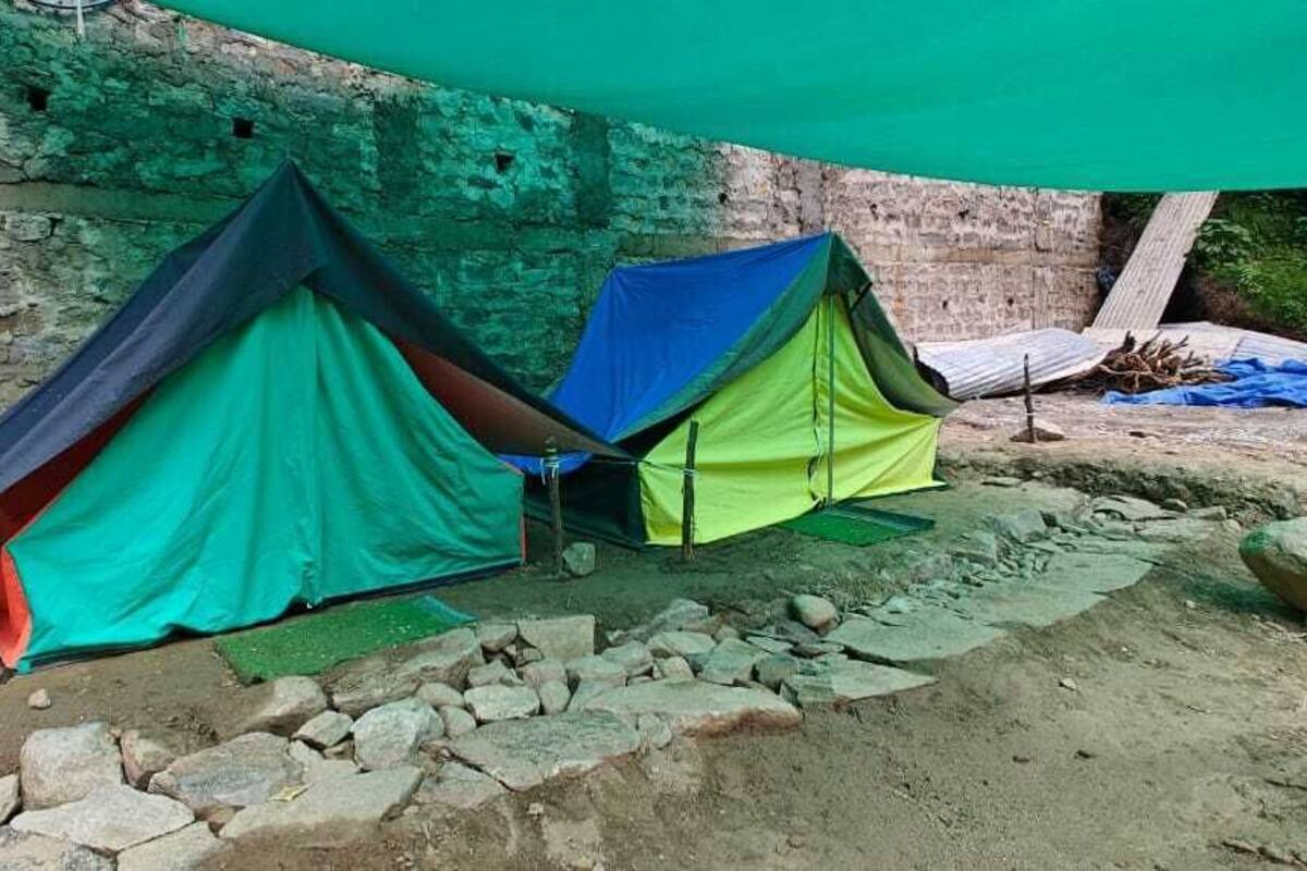 Two tents set up against a brick wall with a rocky ground.