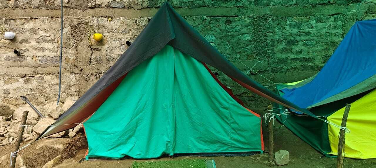 Uma tenda montada em frente a uma parede de pedra, com uma estrutura metálica por perto.