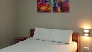 A neatly made bed with white linens and pillows, a wooden headboard, and two wall-mounted paintings. - WJV INN JUGAN (Liloan)