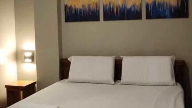 A hotel room with a large bed, two pillows, and three abstract paintings on the wall. - WJV INN JUGAN (Liloan)