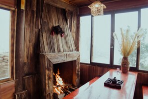 A rustic wooden interior with a fireplace, a wooden bench, and a vase with dried plants. - Muong Hoa River View Homestay (Ta Van)