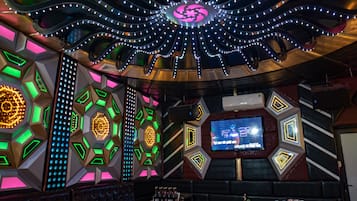 Una habitación con una televisión grande en la pared, diseños geométricos en las paredes y luces colgantes en el techo.