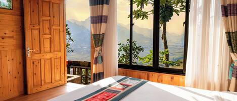 A wooden room with a large bed, a view of mountains, and a balcony with a wooden railing.