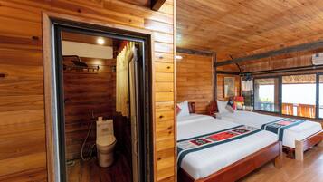 A wooden cabin with two beds, a bathroom, and a large window.