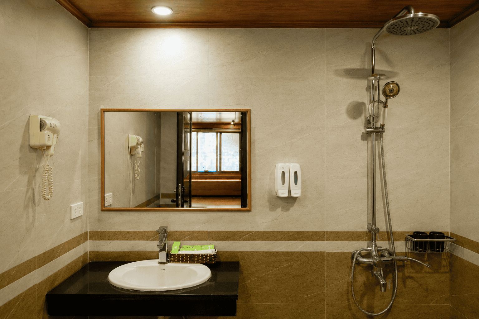 Baño con lavamanos, espejo, ducha y teléfono en la pared.