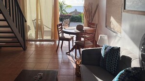 A living room with a sofa, coffee table, and dining table with chairs. There is a staircase on the left and a view of the ocean through the window. - Oceanfront apartment 18 Lagun Blou Resort (Lagun)
