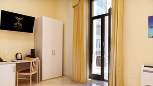 A hotel room with a desk, chair, wardrobe, and a large window with curtains. - Syraka Hotel LR Collection (Syracuse)