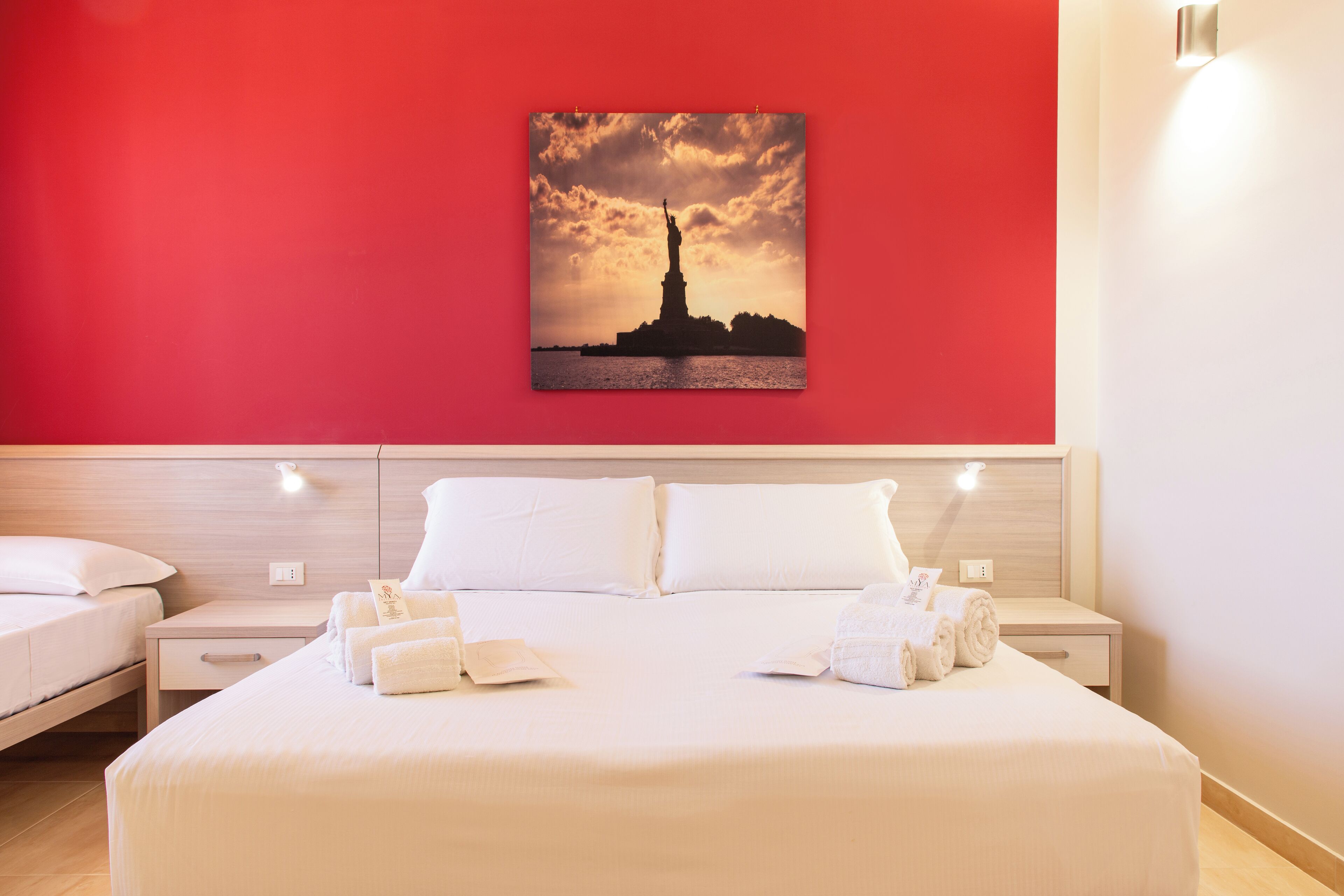 A hotel room with a large bed, two bedside tables, and a wall-mounted artwork of the Statue of Liberty.