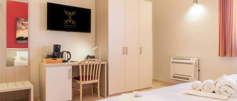 A hotel room with a bed, a desk with a chair, a wardrobe, a television, and a wall-mounted heater.