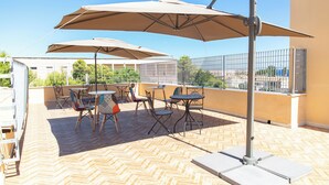 An outdoor patio with tables and chairs, umbrellas, and a view of the city. - Syraka Hotel LR Collection (Syracuse)