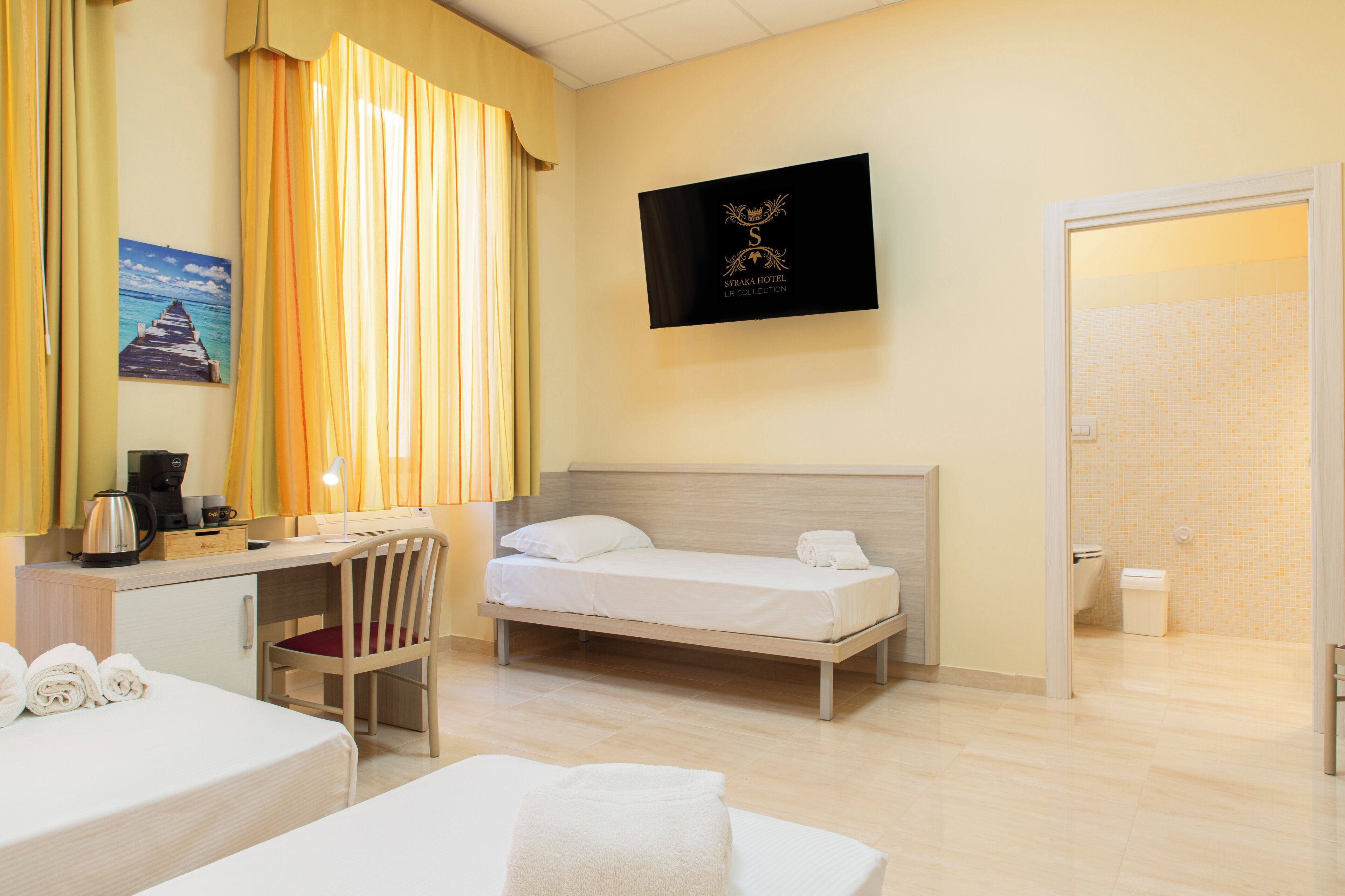 Une chambre d’hôtel avec un lit, un bureau et une chaise, une machine à café et un tableau au mur.