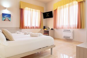 Habitación de hotel con cama, escritorio, silla, televisor y ventana con cortinas.