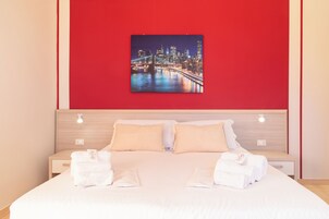 A hotel room with a large bed, two bedside tables, a headboard, and a cityscape painting on the wall.